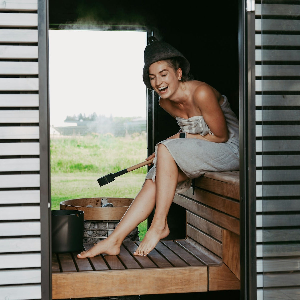 Vrouw ontspant in een moderne privésauna met panoramisch uitzicht op groen landschap.